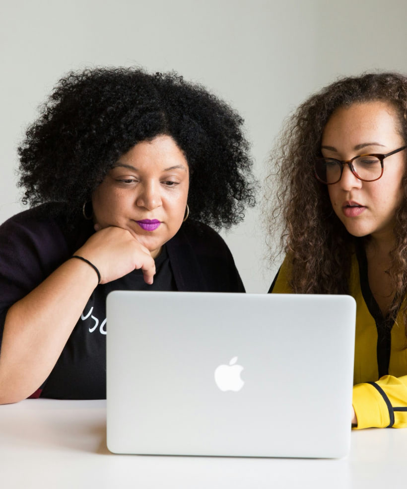 Two women sitting at a table looking at a laptop.